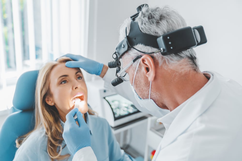 Woman having her throat checked out at the urgent care by an older doctor with a mask on.
