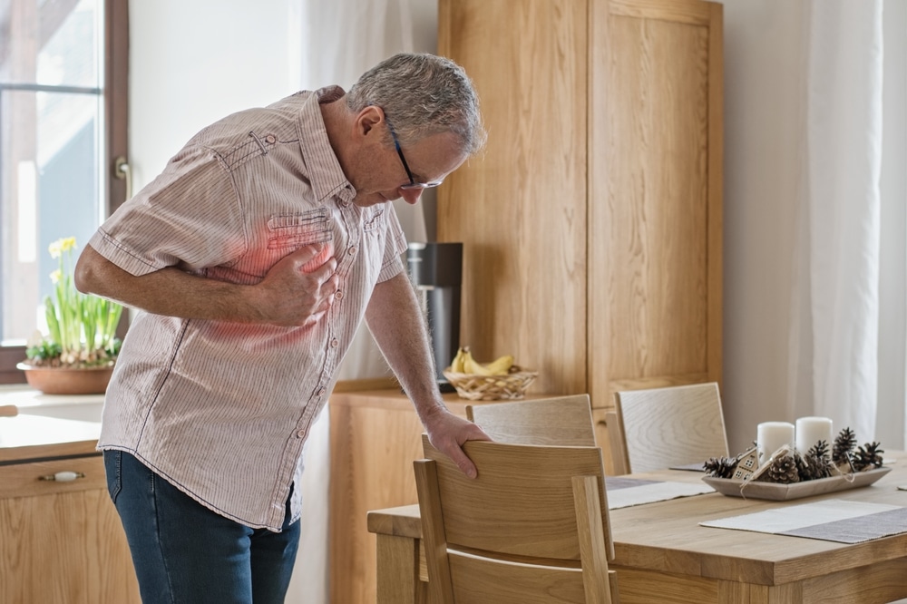 Older man with a hand on his chest, suffering from heart issues related to high cholesterol.