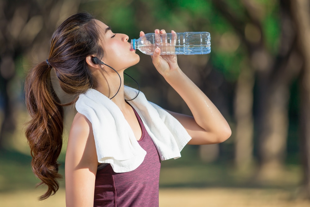 Woman stopping to drink water so she stays hydrated while out on a run.